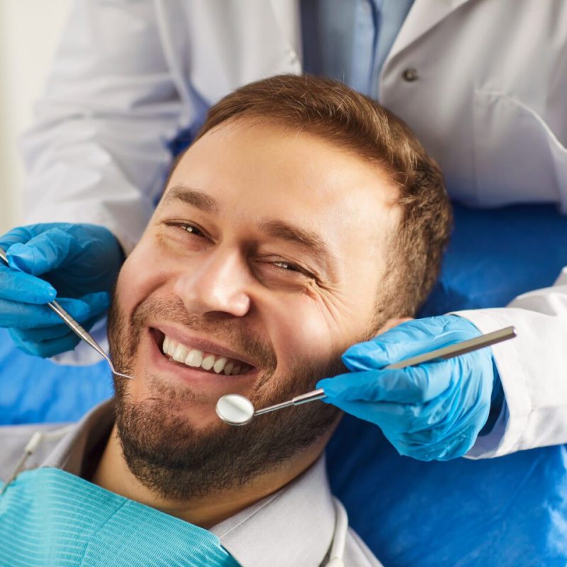 Happy man smiling toothily while being on medical check up in dentistry clinic, undergoes orthodontic dental services, taking care of teeth hygiene, having perfect smile after whitening