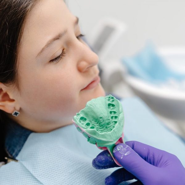 Dentist wearing purple gloves is holding a dental mold of a young patient in a modern dental clinic, ensuring quality oral care