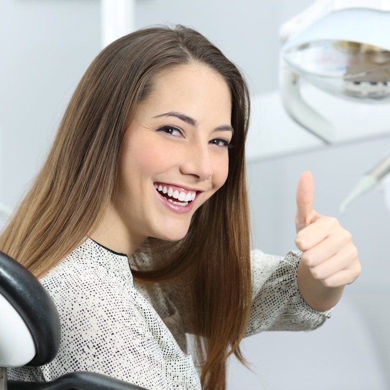 Patient with perfect white teeth and smile satisfied after dental treatment in a dentist office with medical equipment in the background