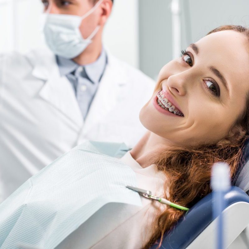 selective focus of beautiful woman in braces during examination of teeth near dentist