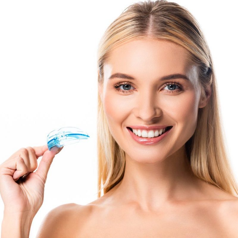 naked happy blonde woman with white teeth holding mouth guard isolated on white