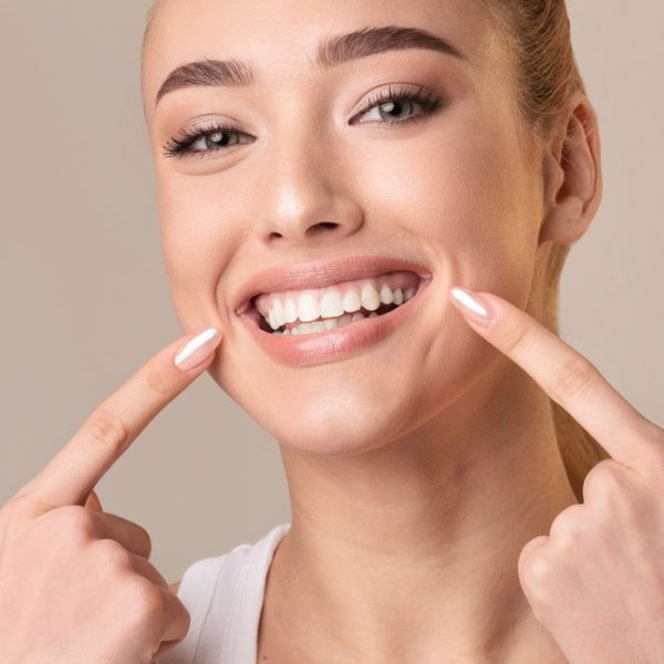 Young Woman Touching Mouth Smiling To Camera On Beige Background Perfect Smile. Young Woman With White Teeth Touching Mouth Smiling To Camera Posing On Beige Background. Studio Shot