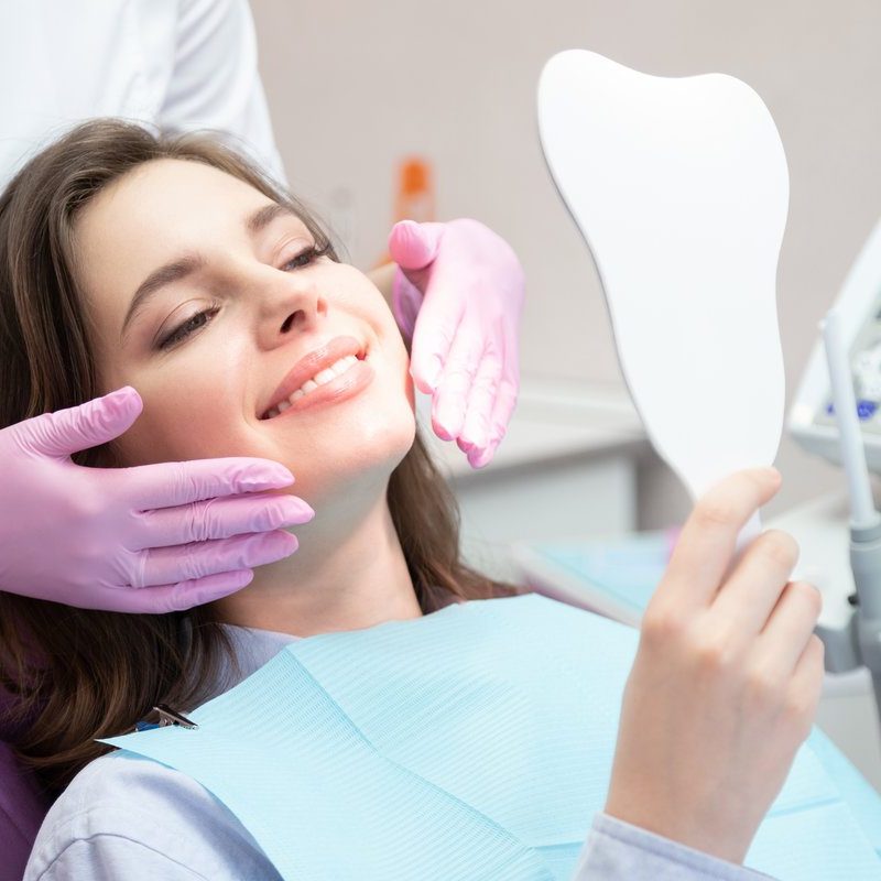 Girl at stomatologist appointment in dental clinic Young glad smiling woman patient looking at mirror after teeth whitening procedure, caries treatment, toothache elimination. Pretty happy girl at stomatologist appointment in dental clinic