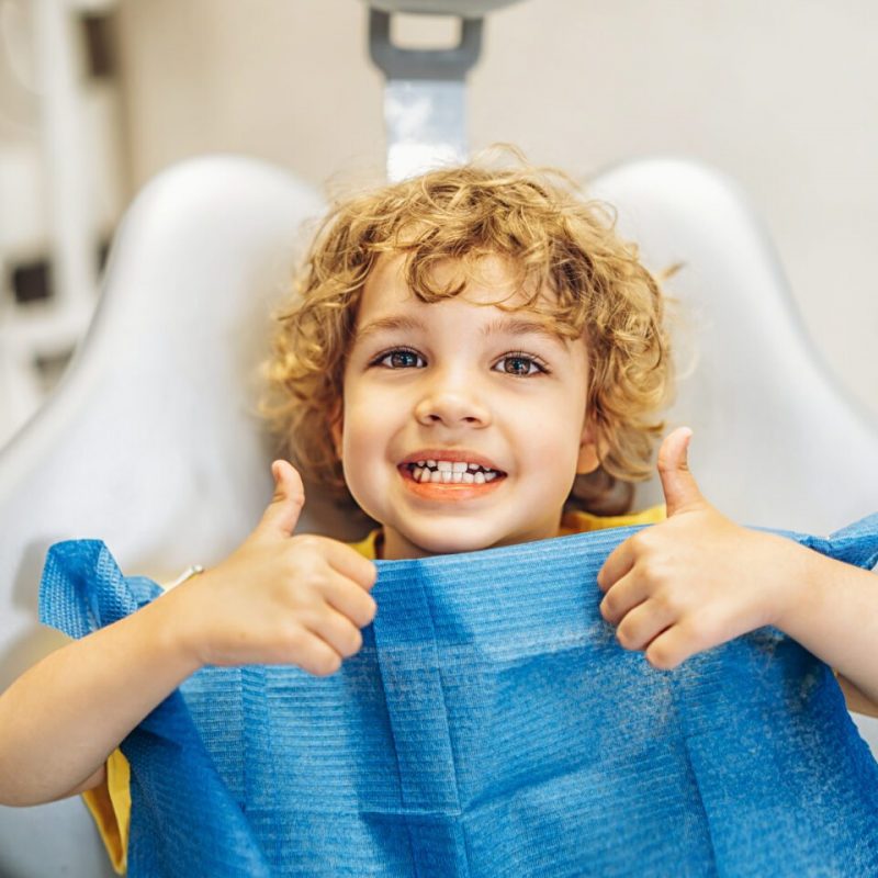 Happy cute little boy in dental ofiice showing thumbs up after treatment