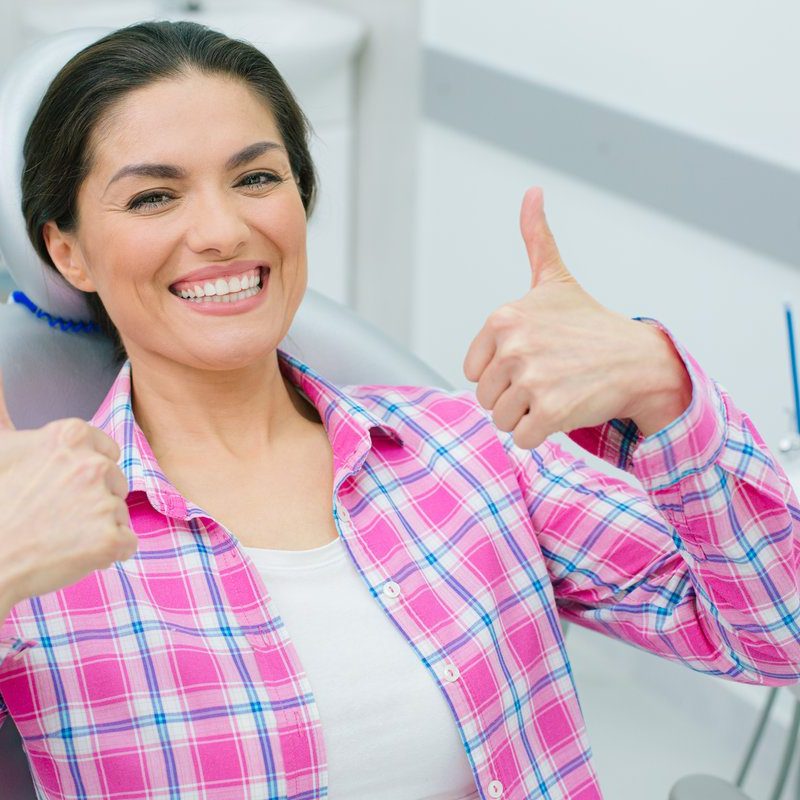 Positive woman revealing her teeth while smiling and showing super gesture with both hands in the dental chair
