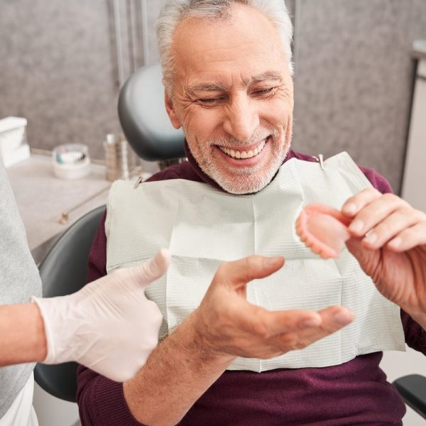 My new teeth. Cropped view of the dentist showing to senior grey haired patient teeth dentures while working at the dental clinic. Man sharing satisfaction smile