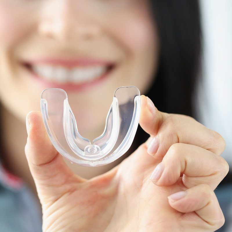 Smiling woman holds transparent plastic mouth guard in her hand. Correction of malocclusion and bruxism concept