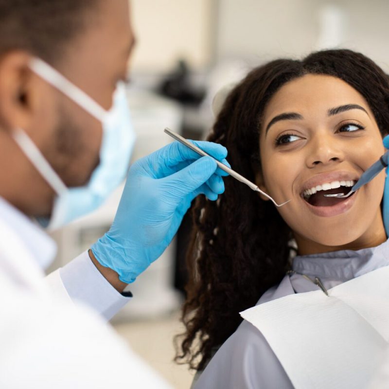 Young African American Woman Having Check Up With Dentist In Modern Clinic, Black Lady Sitting In Chair With Opened Mouth And Looking At Doctor With Dental Tools In Hands, Closeup, Selective Focus