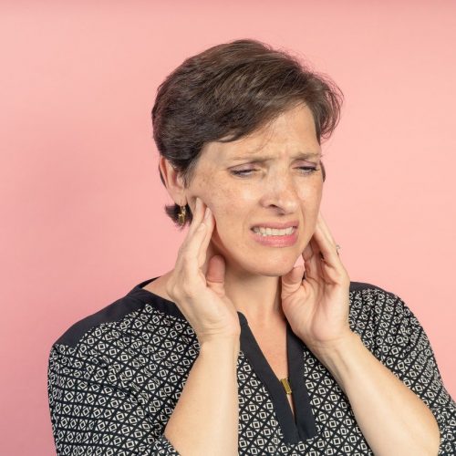 Brunette woman in her 50s in the studio with a pink background with TMJ issues