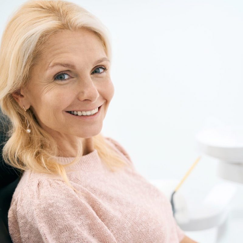 Portrait of happy woman sitting at dental chair and waiting for procedure