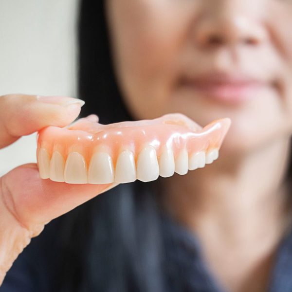 Happy asian woman be smile and holding dentures in hand. Dentures for prosthetic devices constructed to replace missing teeth and helping to chew food.