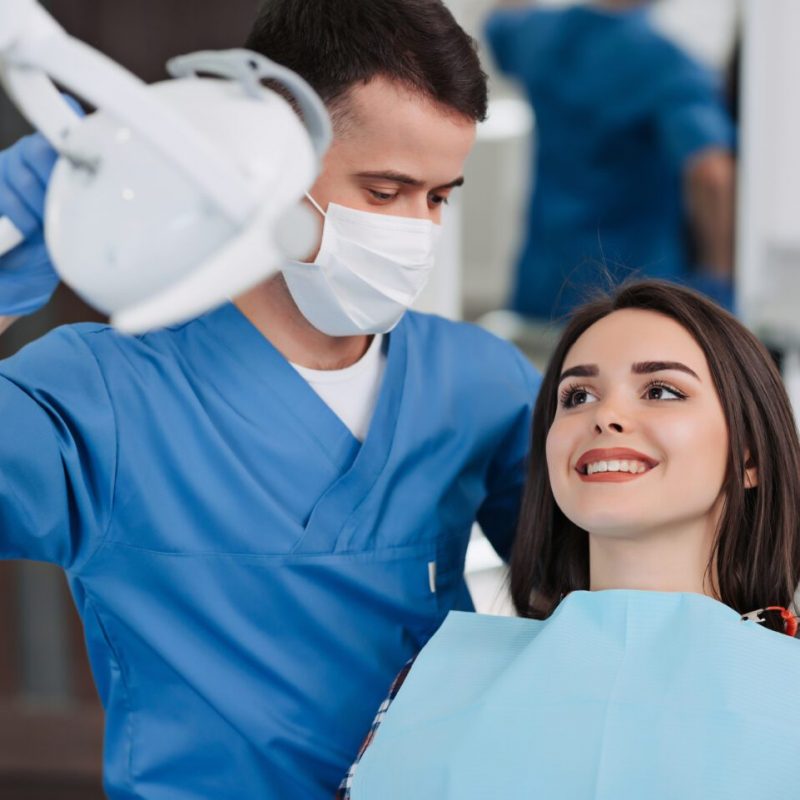 Portrait of executive dentist holding in his hand a lamp and consulting with beautiful patient at dentist office.