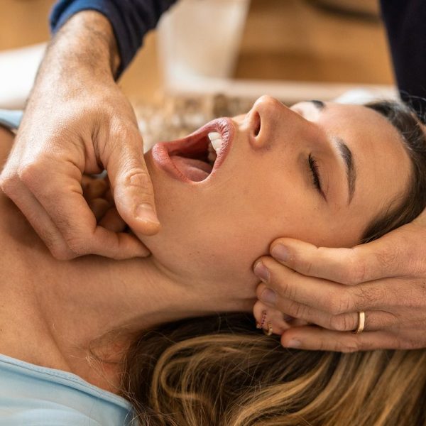 An osteopath performs a jaw adjustment on a female patient, focusing on alleviating tension and improving joint function.