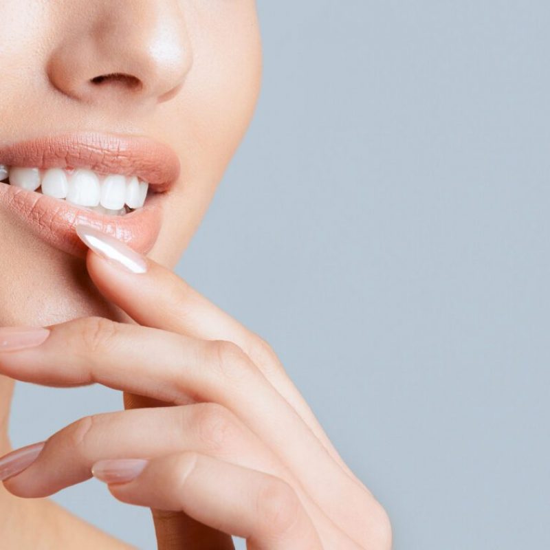 This image shows a close-up of a woman smile and hand. The woman is smiling with her lips parted and her white teeth visible. Her hand is resting on her chin, copy space, cropped